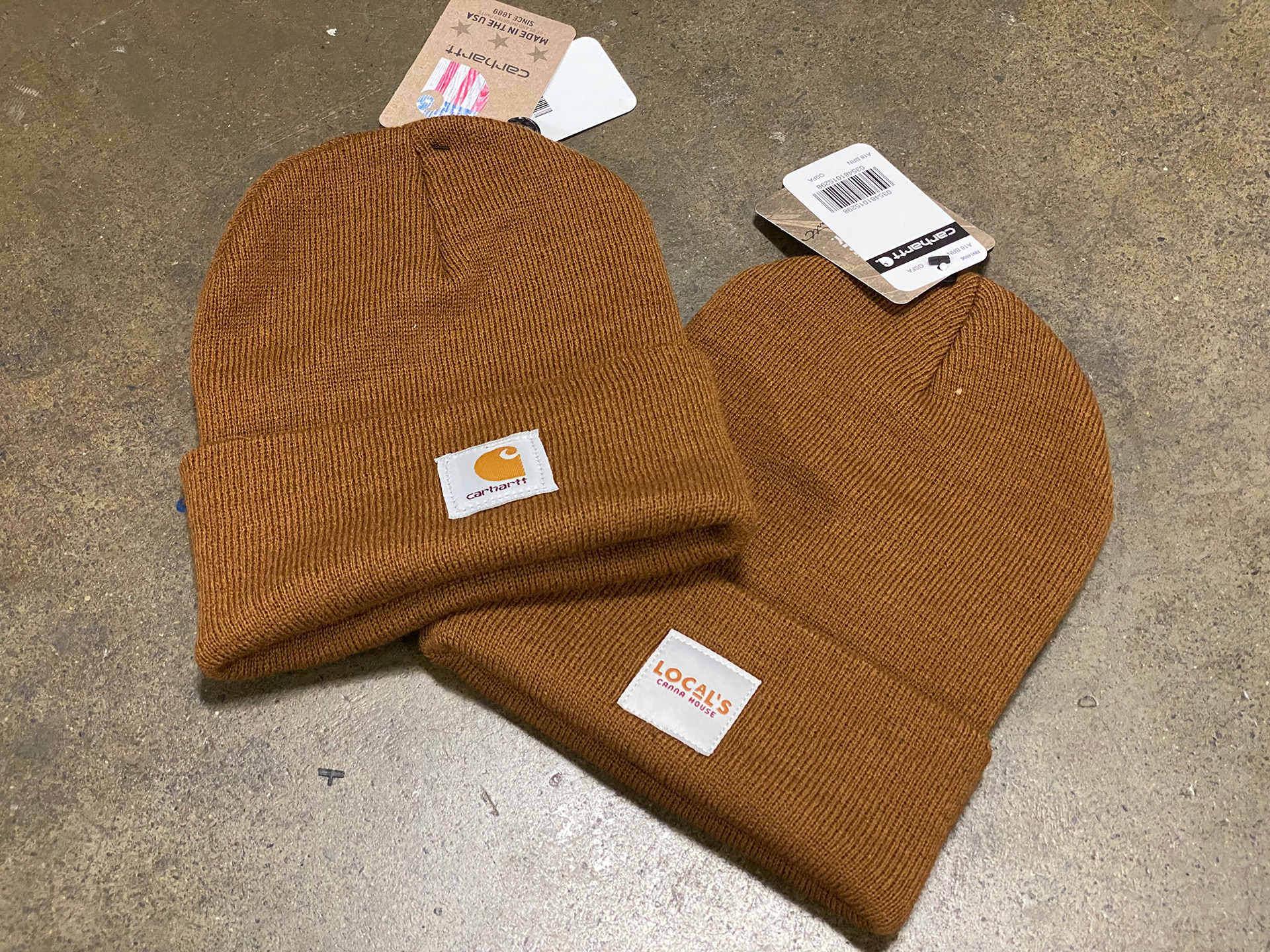 Carhartt beanie with the brand's own woven label next to a matching custom client woven label, same construction and placement