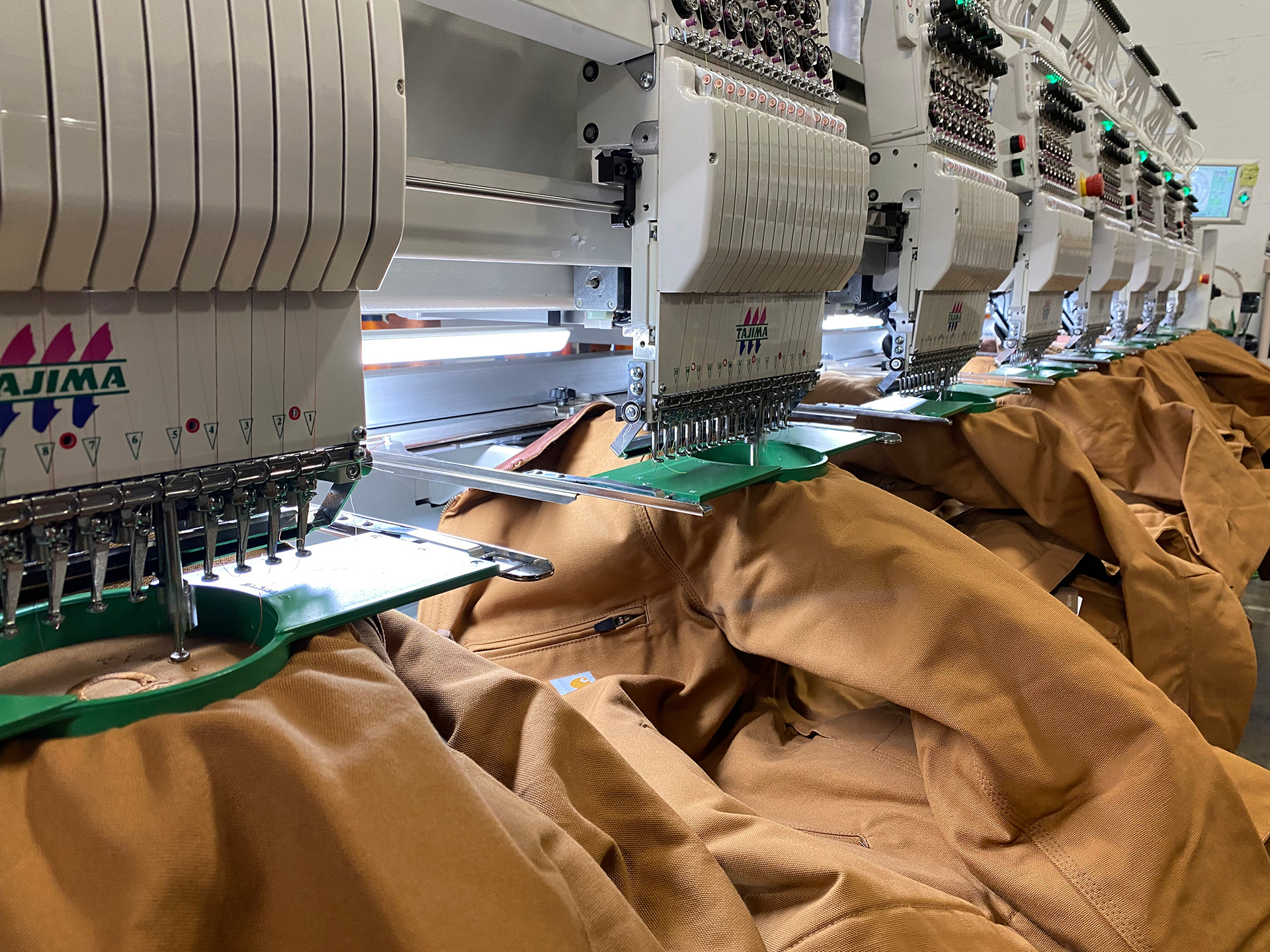 Row of Carhartt jackets hooped in Tajima embroidery machines at Zome Design
