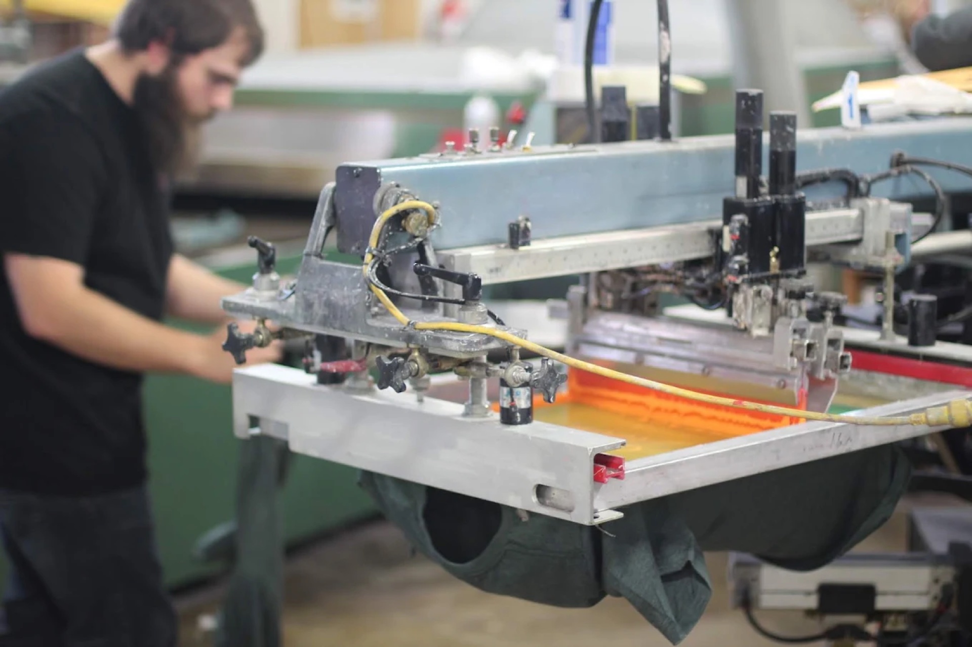Screen printing press loaded with orange ink mid-run on a garment at Zome Design's Spokane Valley shop